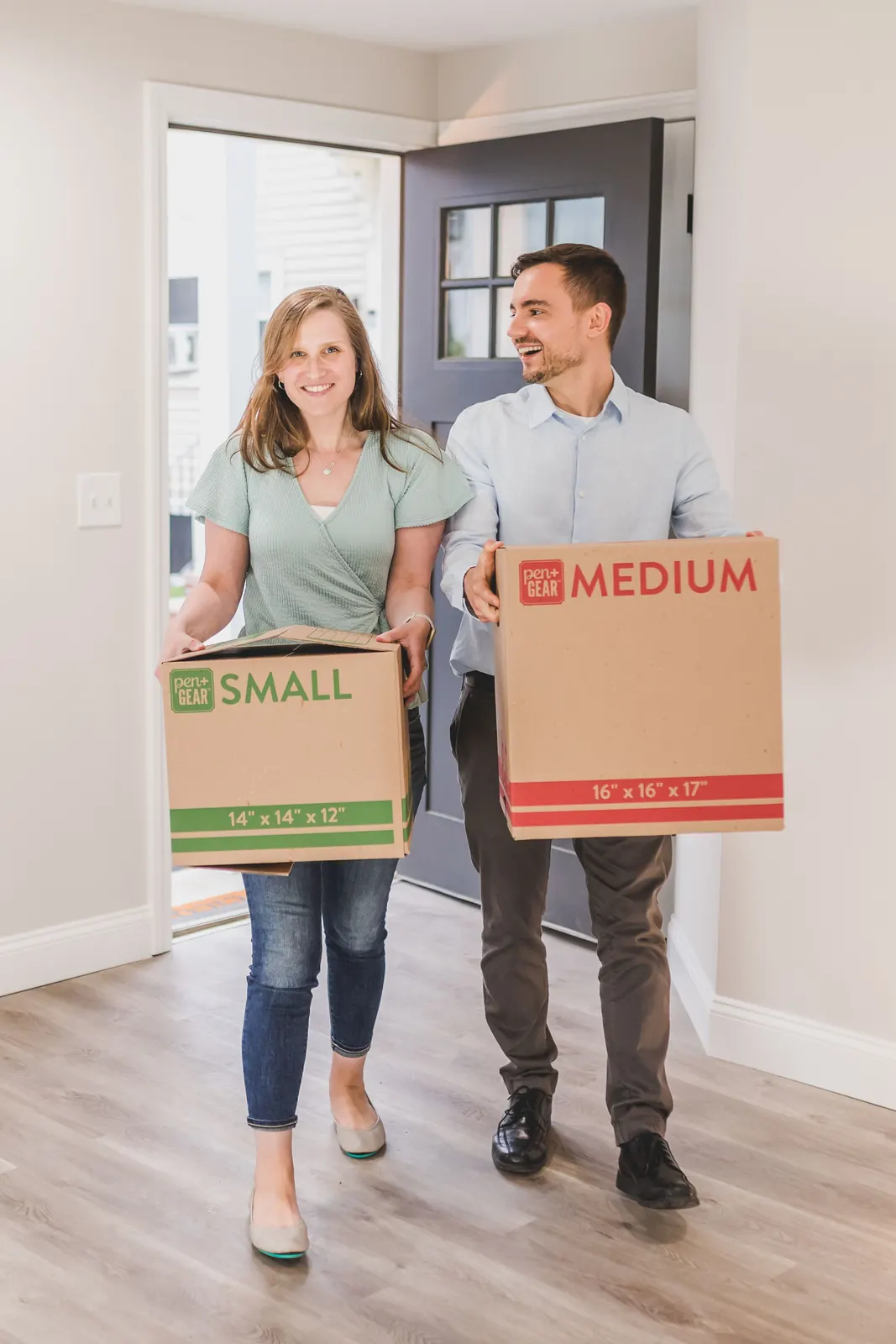 A couple carrying moving boxes through their new front door