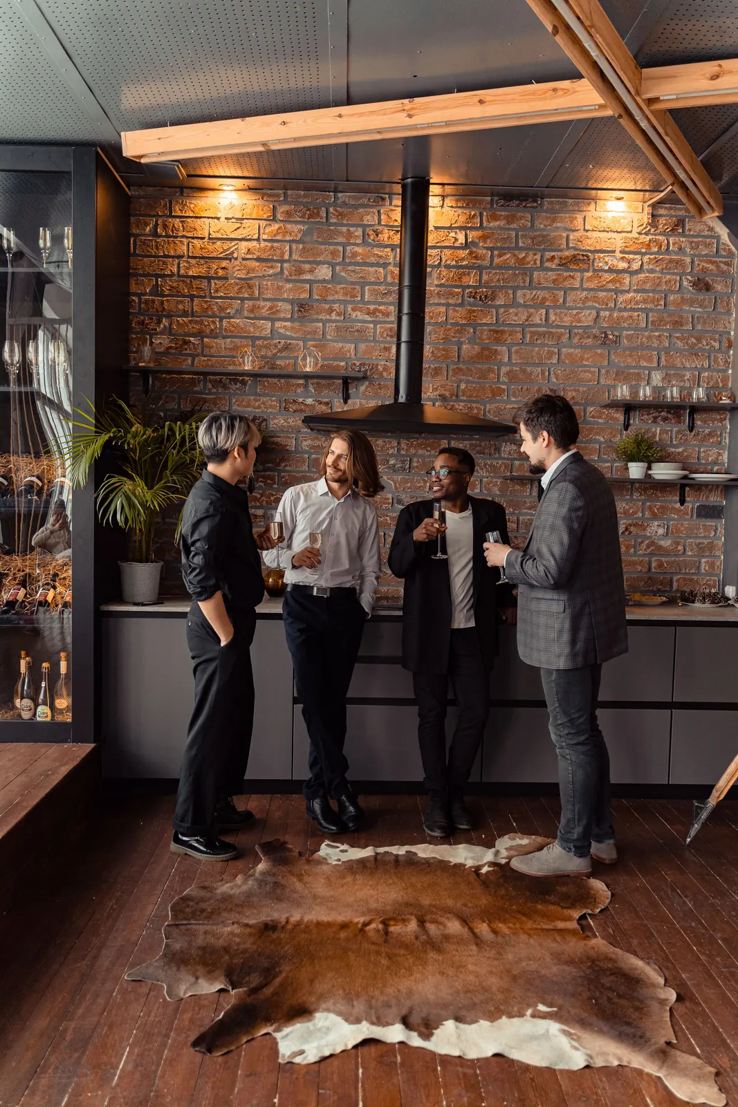 Four friends talking in a kitchen with an exposed brick wall