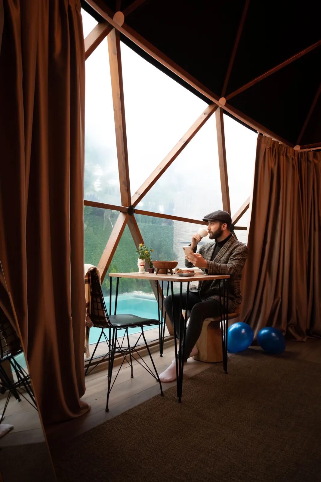 A man at a table inside a glass dome, looking out over the valley