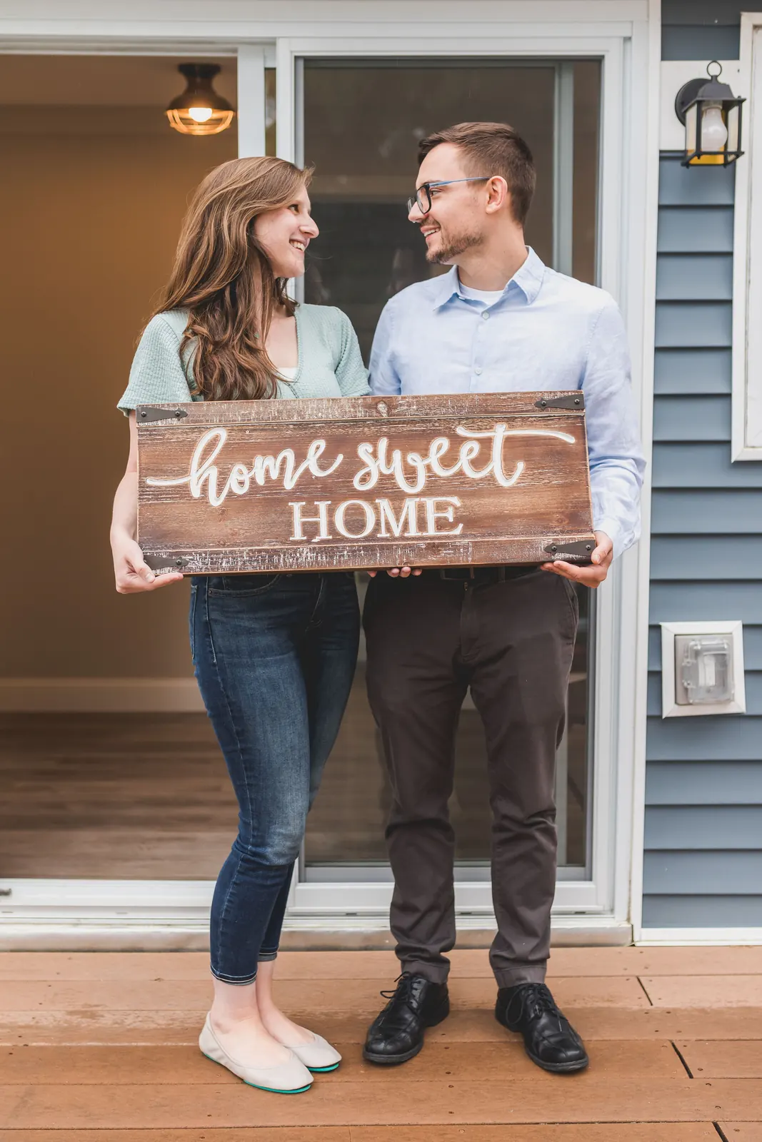 A couple holding a Home Sweet Home sign outside their front door