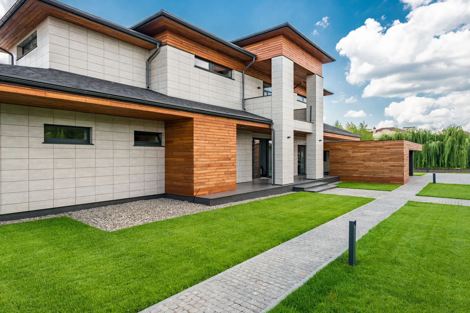 A modern two-storey house with a timber entry and a green lawn