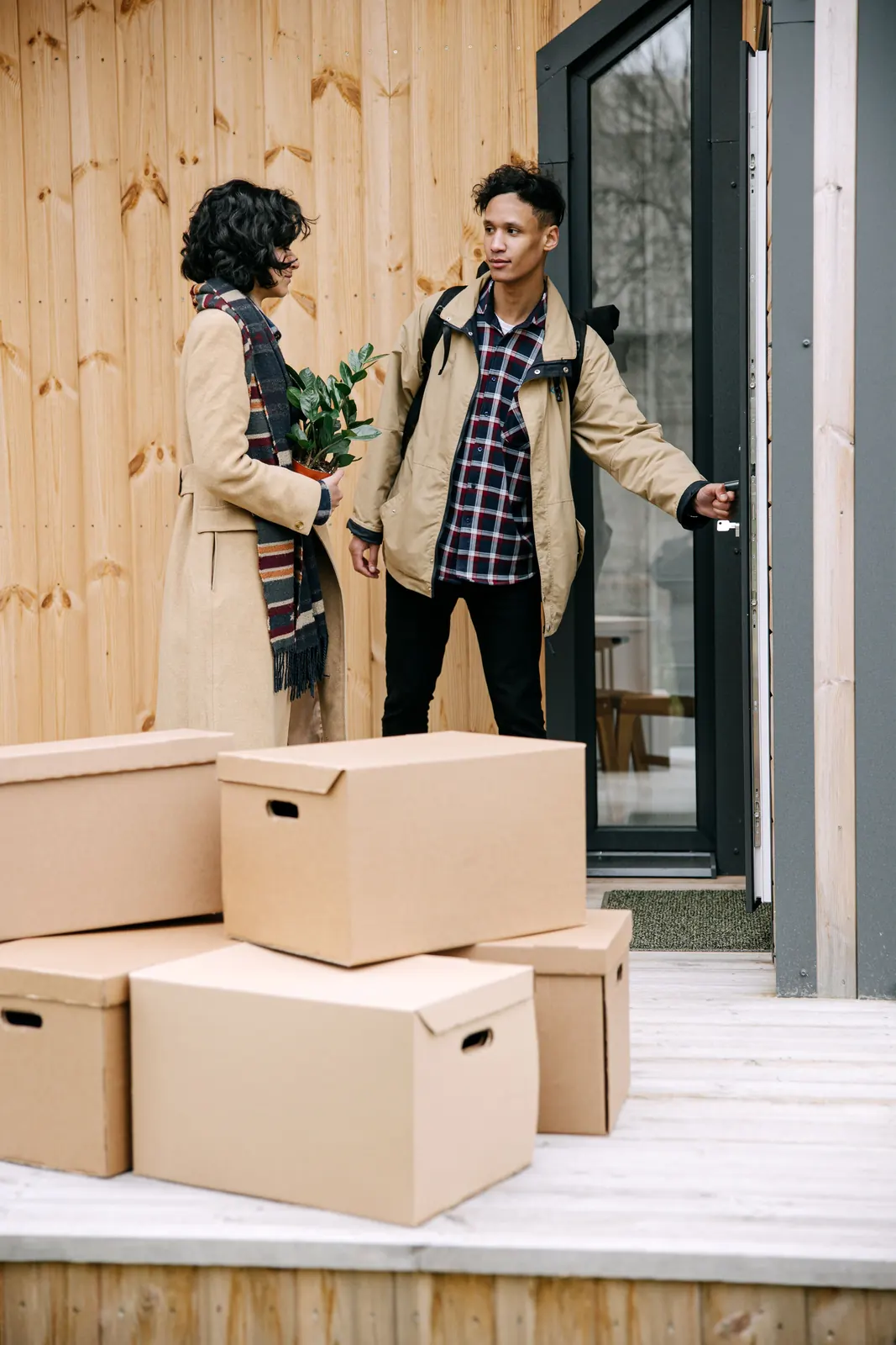 A couple with moving boxes unlocking the door of a timber house